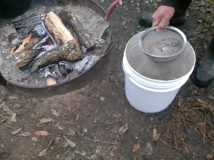 sifting wood ashes into plastic bucket